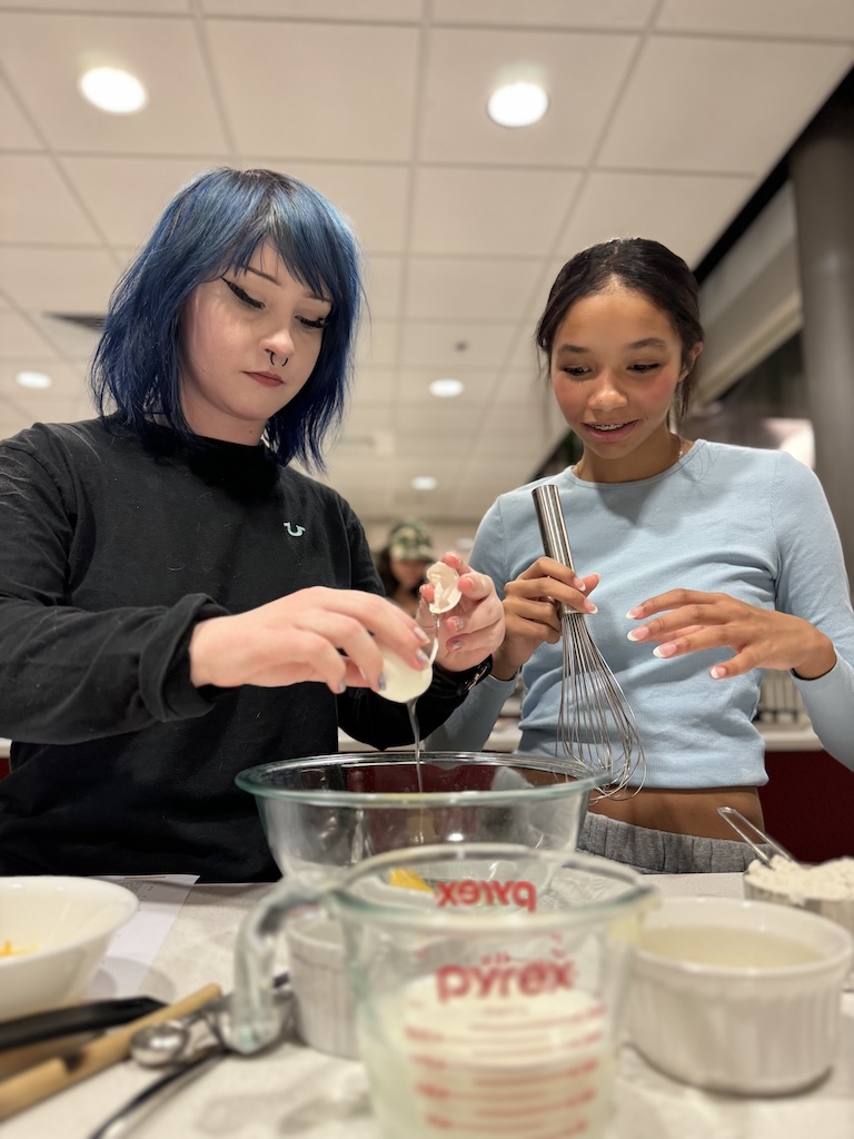 Two girls adding ingredients to a glass bowl