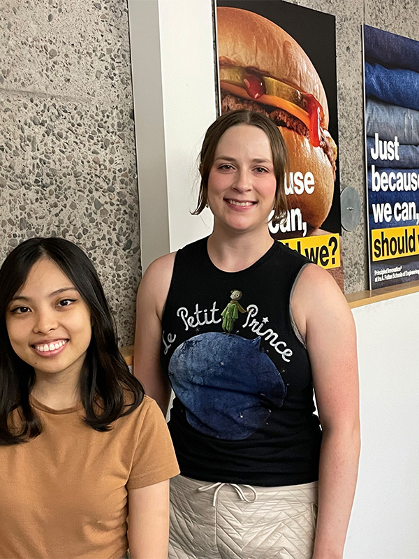 Two students stand in front of a poster depicting a hamburger, with the words