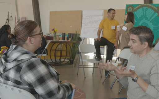 Two people seated in folding chairs engaged in animated conversation