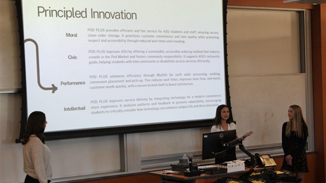 Three students stand in front of a projector screen that reads 'Principled Innovation'