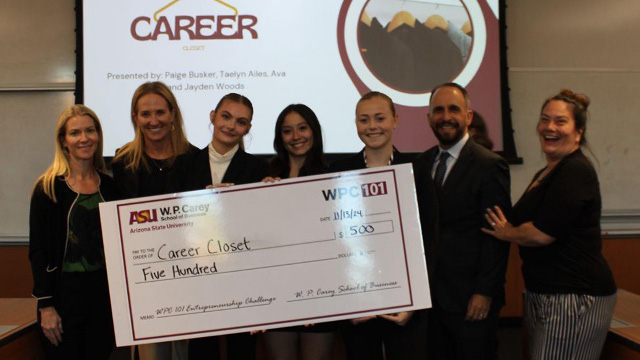 Seven people smile as they stand and hold a giant check for $500