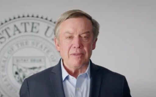 ASU President Michael Crow speaking in front of a white wall featuring the university seal.
